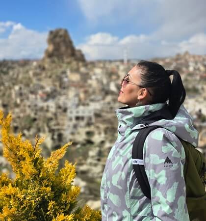 Ortahisar Kapadokya manzarasına karşı duran bir ziyaretçi; arka planda Ortahisar Kalesi ve taş evlerle panoramik görünüm